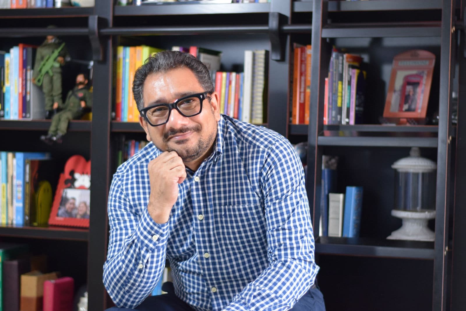 Enzo Borges sorrindo, com a mão no queixo, em frente a uma estante de livros